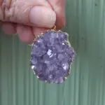 Hand holding a purple crystal pendant.