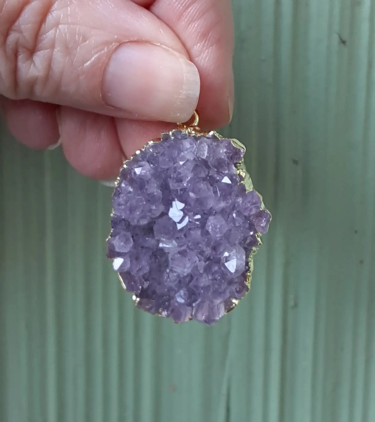 Hand holding a purple crystal pendant.