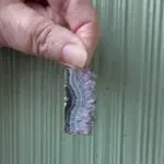 Hand holding a small rectangular gemstone slice.