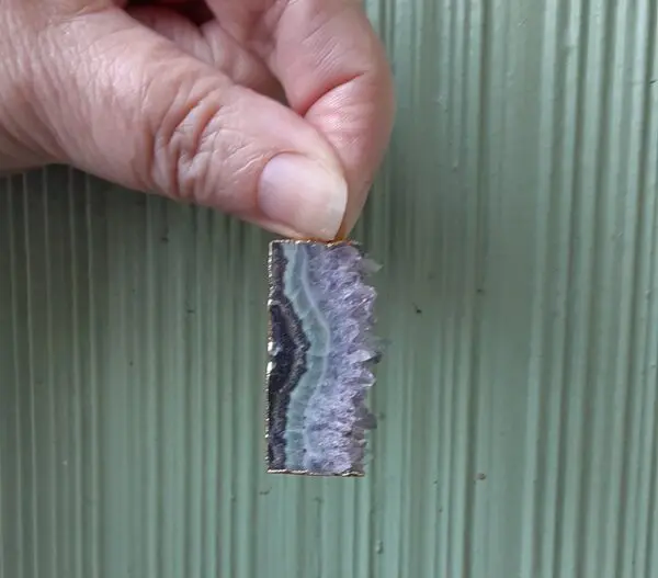Hand holding a small rectangular gemstone slice.