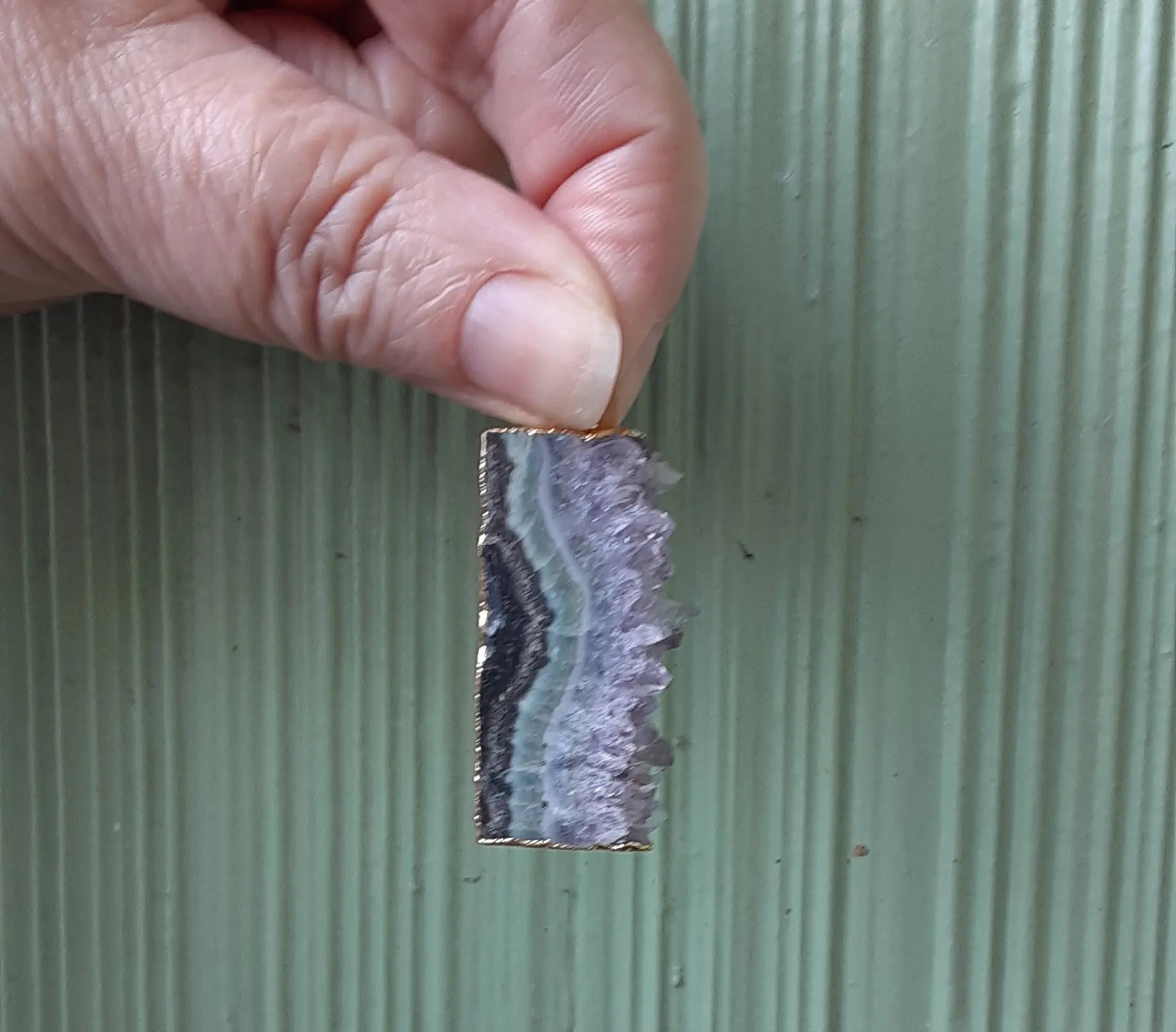 Hand holding a small rectangular gemstone slice.