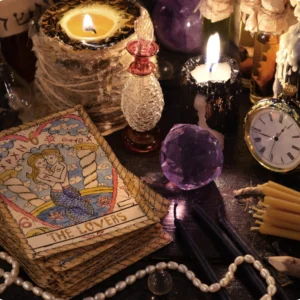 A tarot card reading setup with "The Lovers" card, candles, a pocket watch, crystals, and beads on a dark surface.