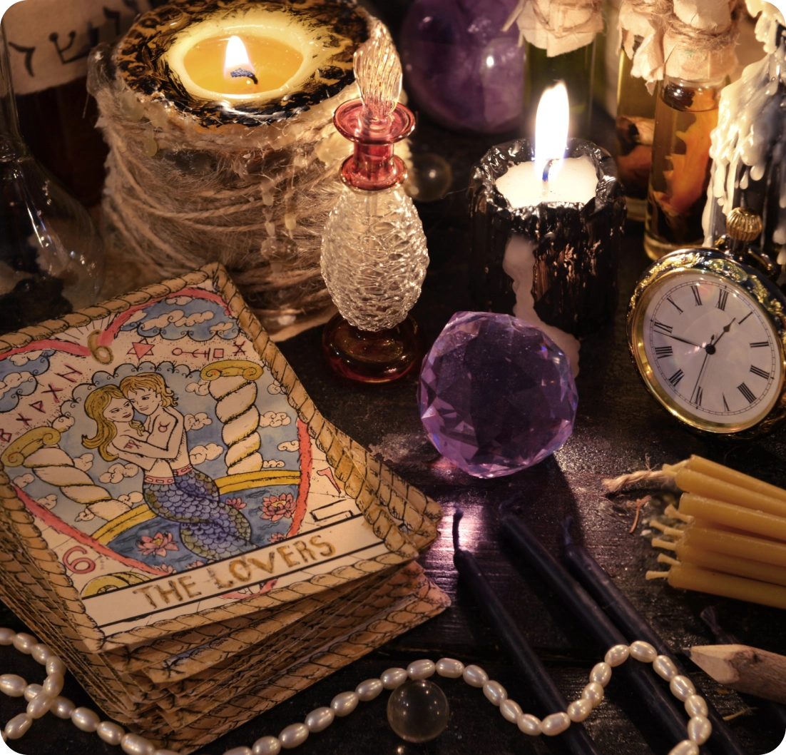 A tarot card reading setup with "The Lovers" card, candles, a pocket watch, crystals, and beads on a dark surface.